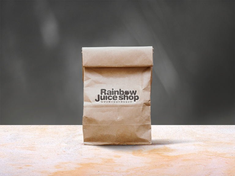 『Rainbow Juice Shop(レインボージュースショップ)』のロゴがプリントされたクラフト紙のテイクアウトバッグ。シンプルでエコフレンドリーなデザインが特長で、ナチュラルな風合いがブランドのフレッシュなイメージを引き立てる。