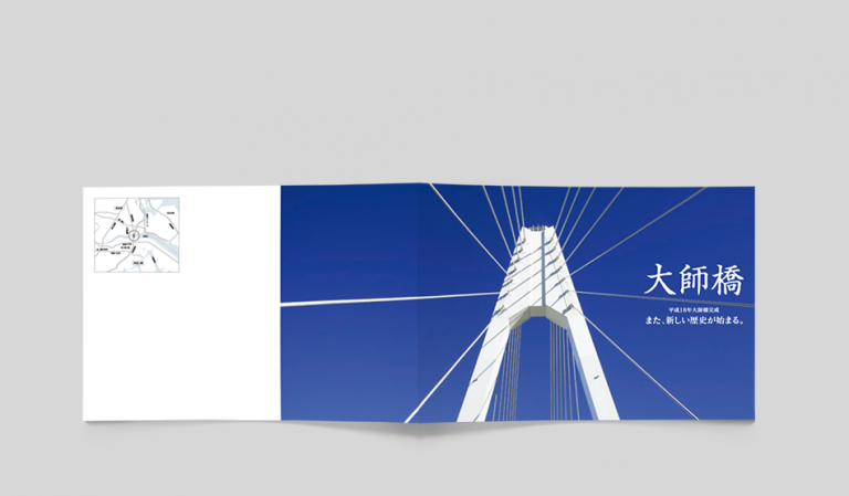 大師橋架替え工事の竣工記念パンフレット。A4横サイズのデザインで、青空を背景にそびえ立つ大師橋の主塔がダイナミックに表現されている。橋梁の圧倒的な存在感を強調し、新たなランドマークの完成を記念する構成。