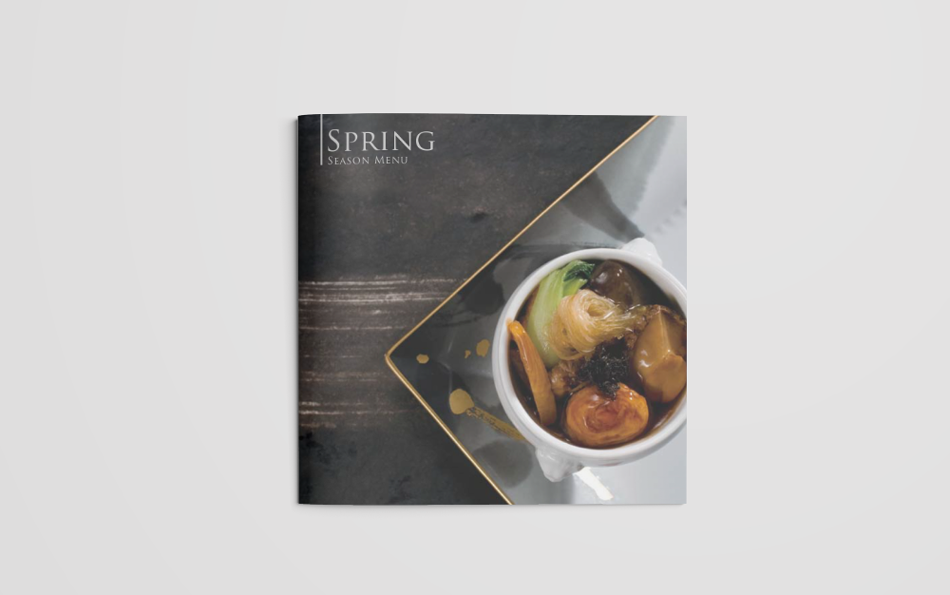 高級感のある黒いプレートに置かれた、白い器に盛り付けられた春の季節限定メニュー。フカヒレ、鮑、椎茸、青梗菜、人参などの食材が濃厚なソースとともに調理され、贅沢な一皿を演出。金の縁取りが施されたプレートが洗練された雰囲気を醸し出し、ホテルレストランの春のグルメプロモーションに最適なデザイン。